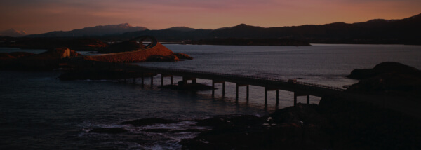 Verschwommene Küstenlandschaft mit einer Brücke bei Sonnenuntergang.